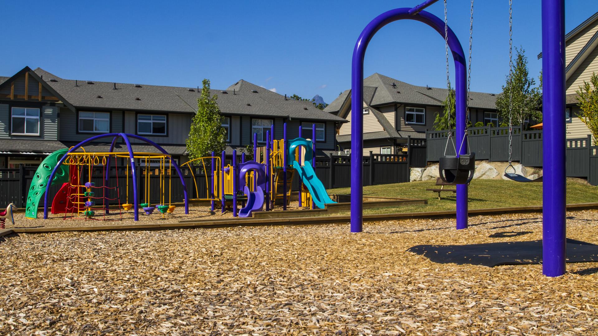 The swing set is in front of the playground, which is by some houses.